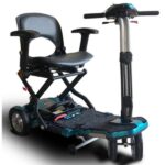 A compact, foldable mobility scooter with a black seat and armrests, mounted on a lightweight frame with small wheels. The scooter features handlebars for steering and has a foot platform. The frame and seat are mainly black, with some metallic and blue accents.
