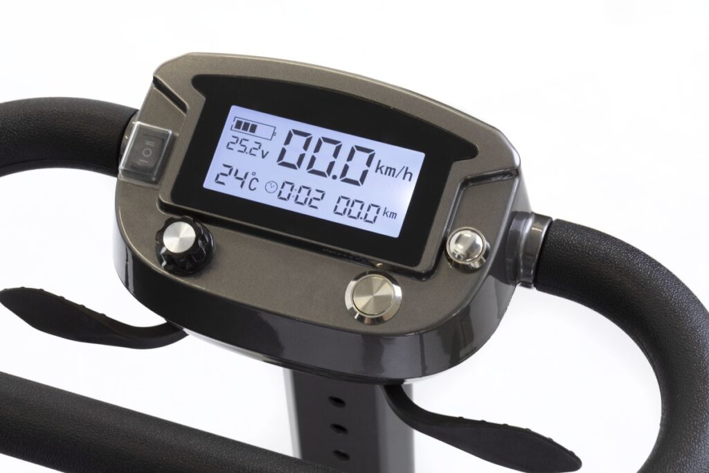 A close-up of a mobility scooter control panel with a hand operating it, displaying battery level and speed settings.