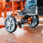 Operator foot pressing the parking brake pedal between the 8 inch solid wheels of the SuperHandy GUO097 material lift