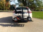 Go Go scooter riding on the Model 210 behind a sedan outdoors